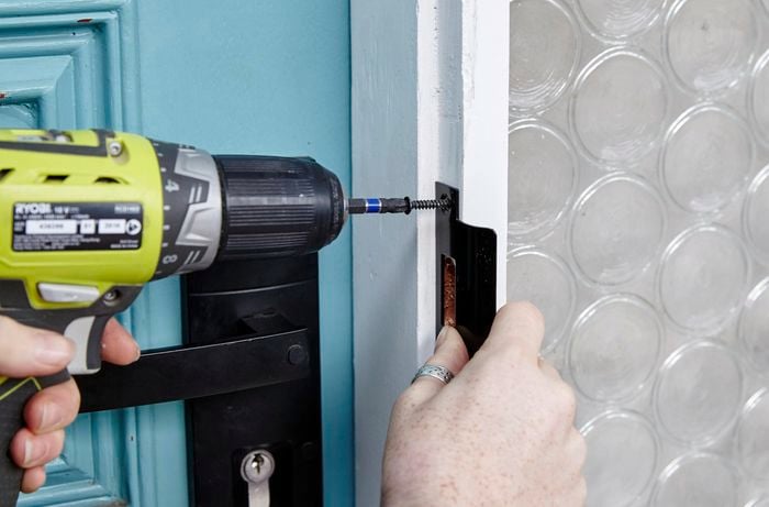 A striker being secured to the door frame with a power drill