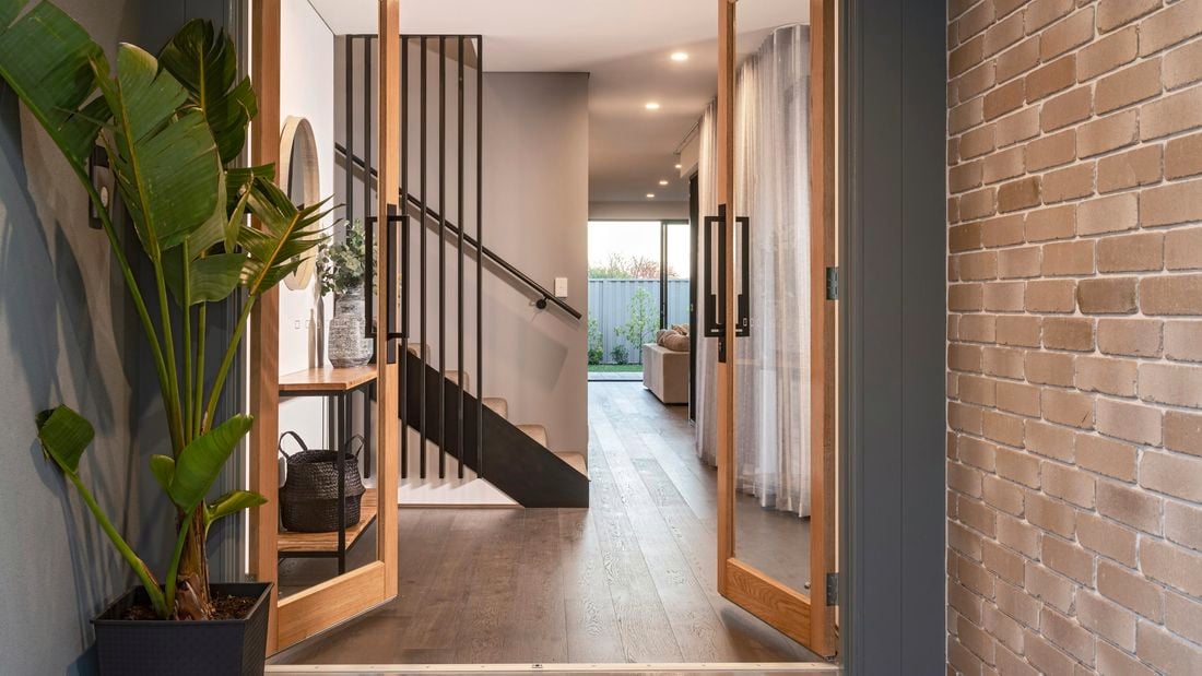 Double glass doors with timber frame opening up into a house with stairwell and living area with matte black door hardware