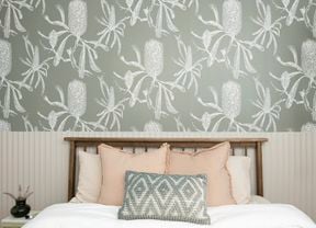An image of a tidy room with a bed, a bedside table and modern wallpaper in the background