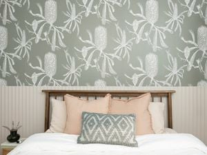 An image of a tidy room with a bed, a bedside table and modern wallpaper in the background