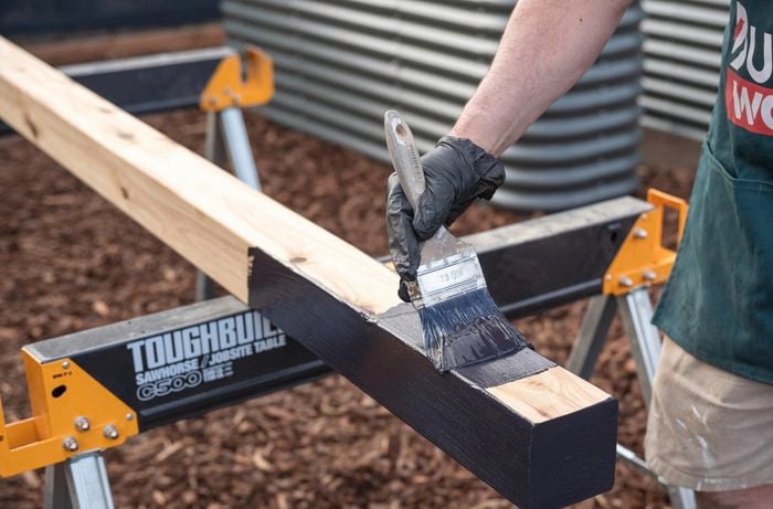 A Bunnings Team Member holding a paint brush against a timber post with Bitumen paint on it