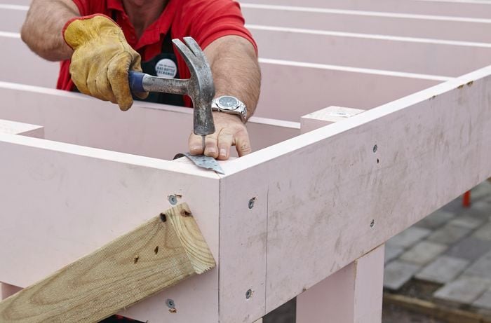 Person hammering a hoop iron to a carport frame.