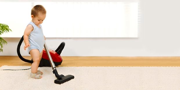Baby using a vacuum on a rug.