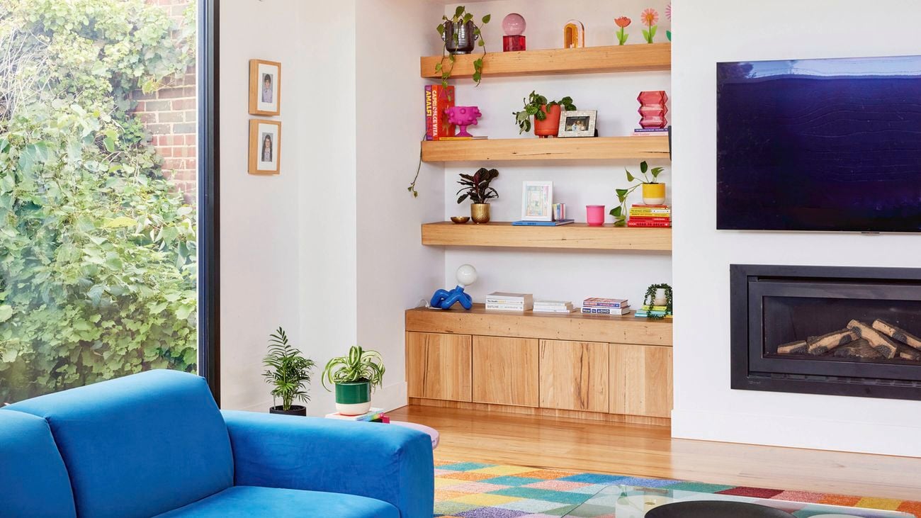 Natural light living room featuring neurodivergent interior design elements, a blue sofa, colourful rug, wooden shelving with organised displays and calming greenery