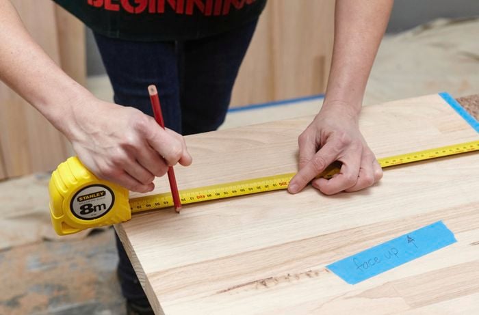 A person marking a measurement onto a timber panel using a measuring tape