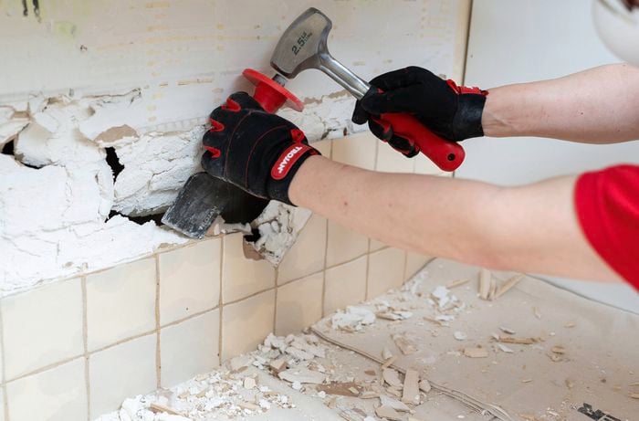 Person removing remaining wall tiles using hammer and chisel