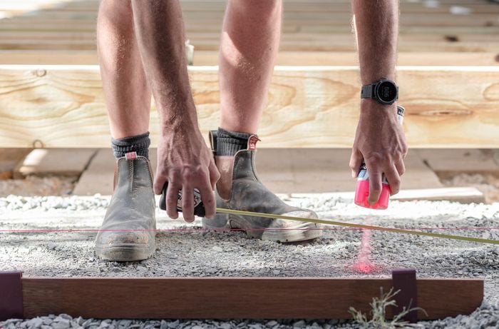Person using a string line and fluoro paint with a tape measure to mark out paver positions.