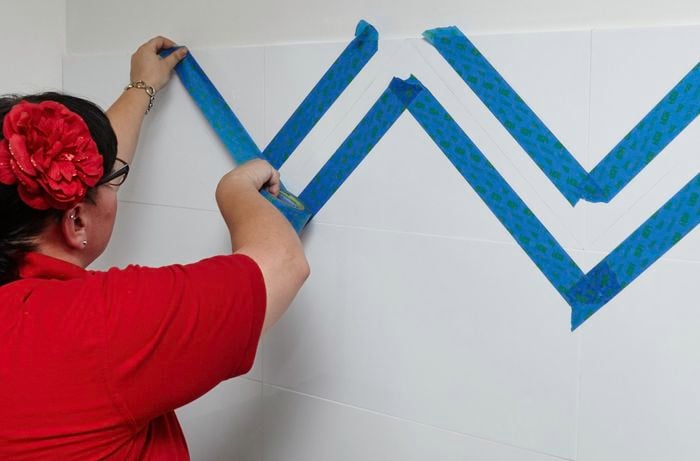 A person applying masking tape to splashback tiles in a zig-zag pattern