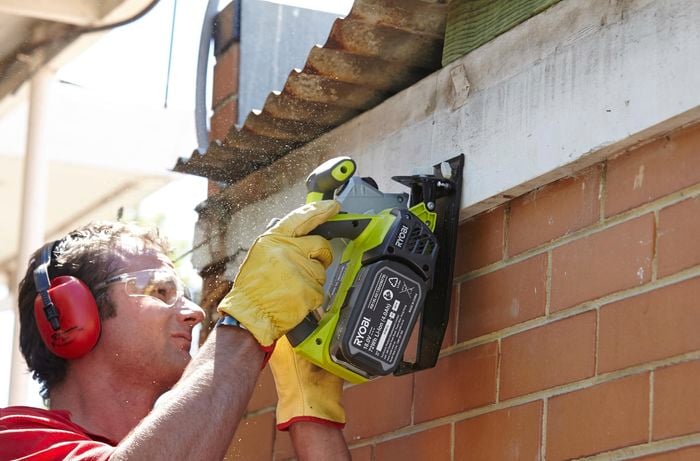 A person wearing protective gear cutting a fascia board using a circular saw