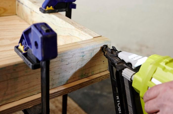 A person using a nail gun to assemble a timber frame