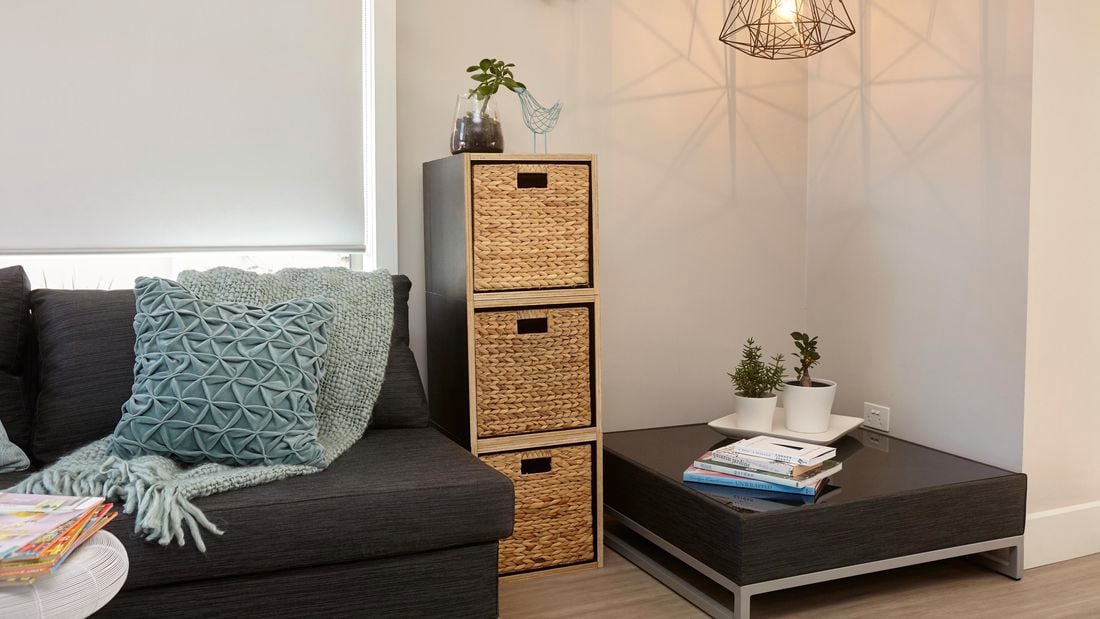 A wooden storage box with three wicker baskets in a warmly lit lounge room setting next to a modern black coffee table