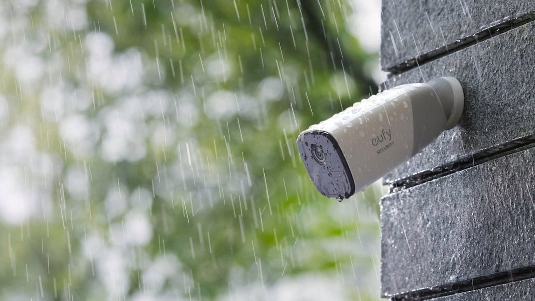 eufy security camera outside mounted to a gray wall in the rain.