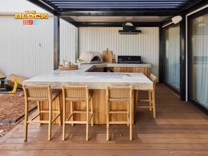An outdoor area with a kitchen bench, with a pizza oven, barbecue on it and chairs in front of it.
