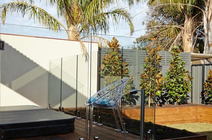 A completed glass pool fence installed around a spa deck in a backyard