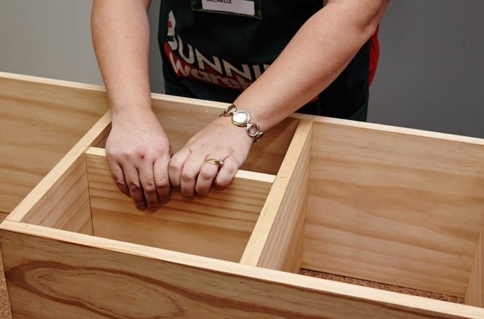 Storage shelves being fitted inside a frame on a kids storage bench by a Bunnings team member