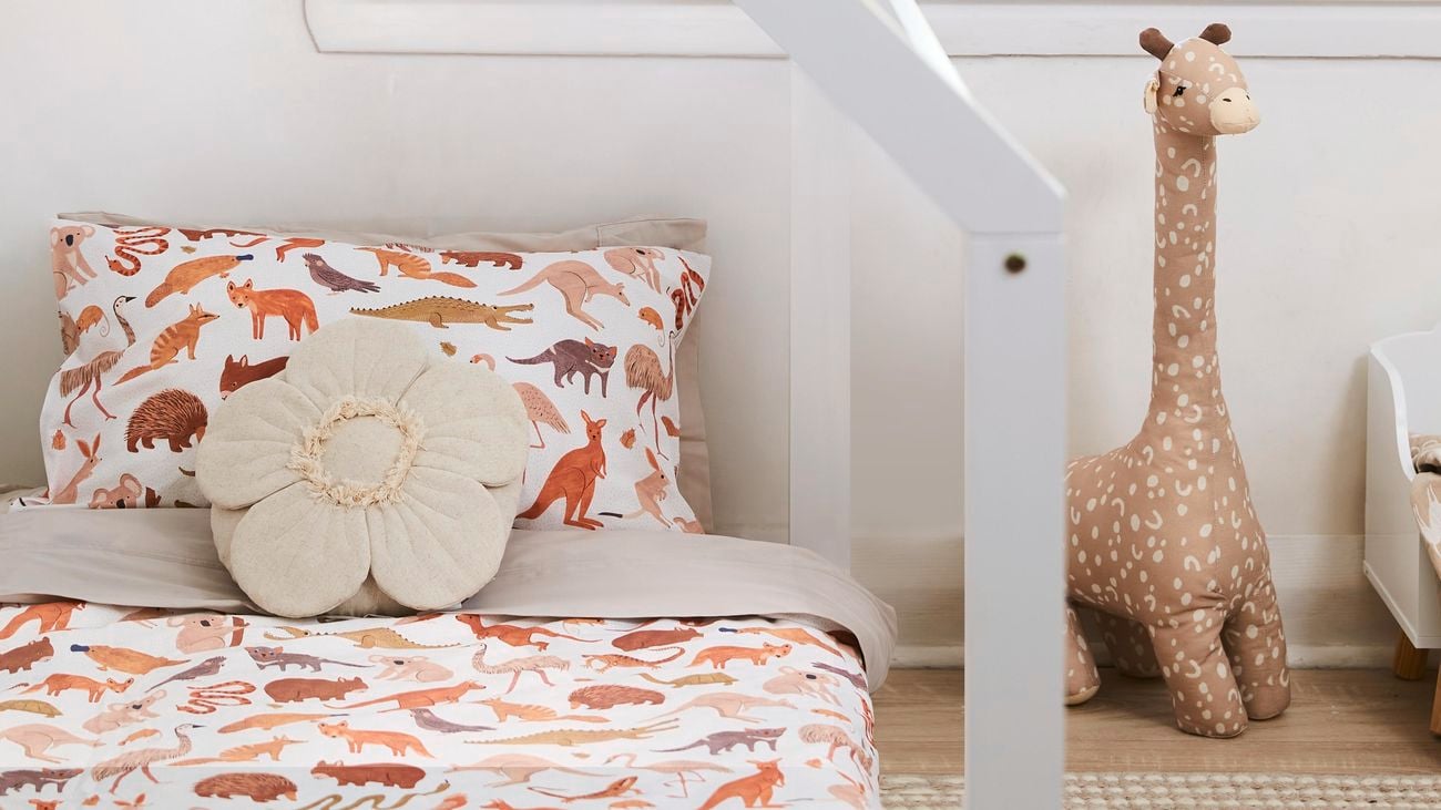Timber kids house bed with animal printed sheets and a plush giraffe