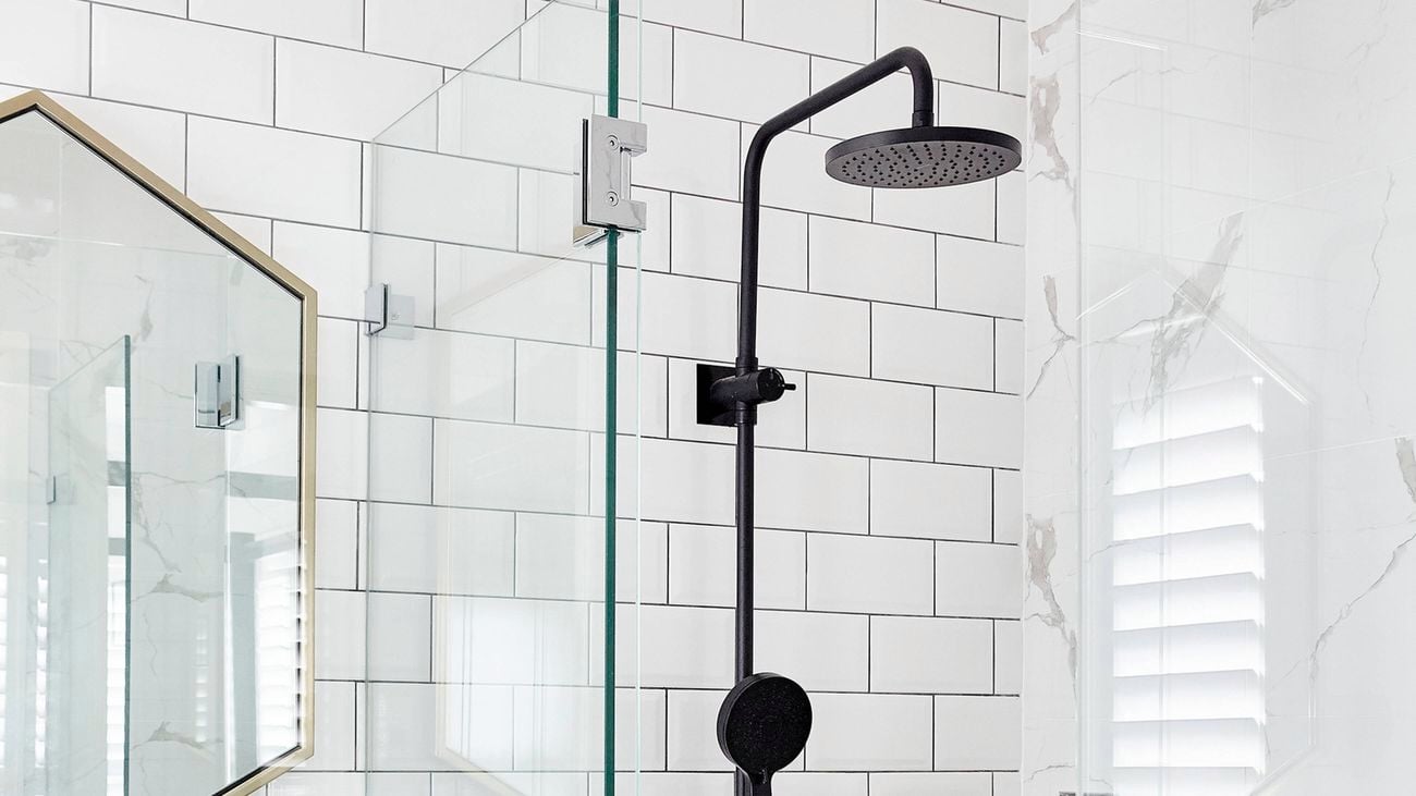 Shower with white tiles, black showerhead, bathroom mirror and glass screen.