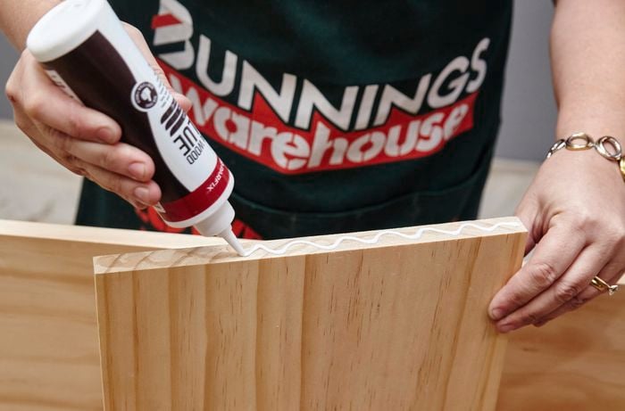 Wood glue being applied to a timber shelf panel in a zigzag pattern