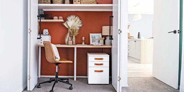 Office space with a desk inside a closet, leather office chair and white set of drawers.