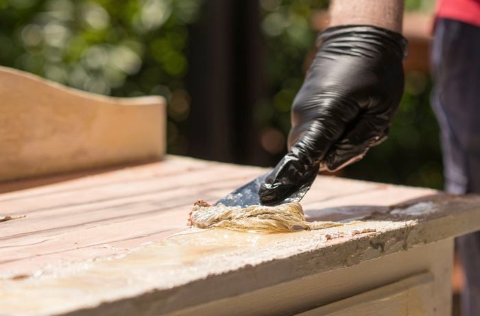 Scrape away the paint from a wooden surface using a scraper 