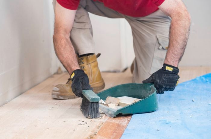 A person is cleaning the floor and removing leftover screws, debris and dust.  