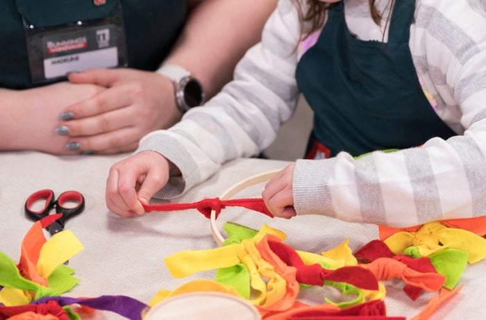 A kid is tying felt strips to a wooden wreath frame