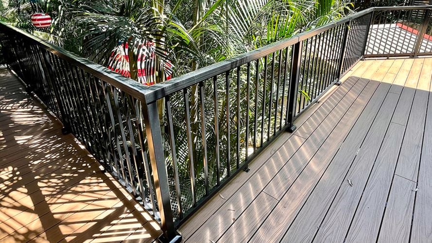 Top down view of the balcony overlooking trees, with a black aluminium balustrade and wooden flooring.