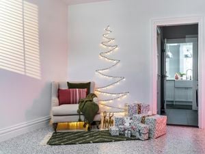 A tree against a wall made of fairy lights in a lounge room