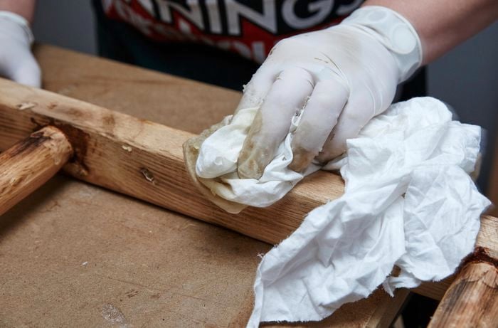 Person wiping DIY timber vintage ladder with rag and varnish.