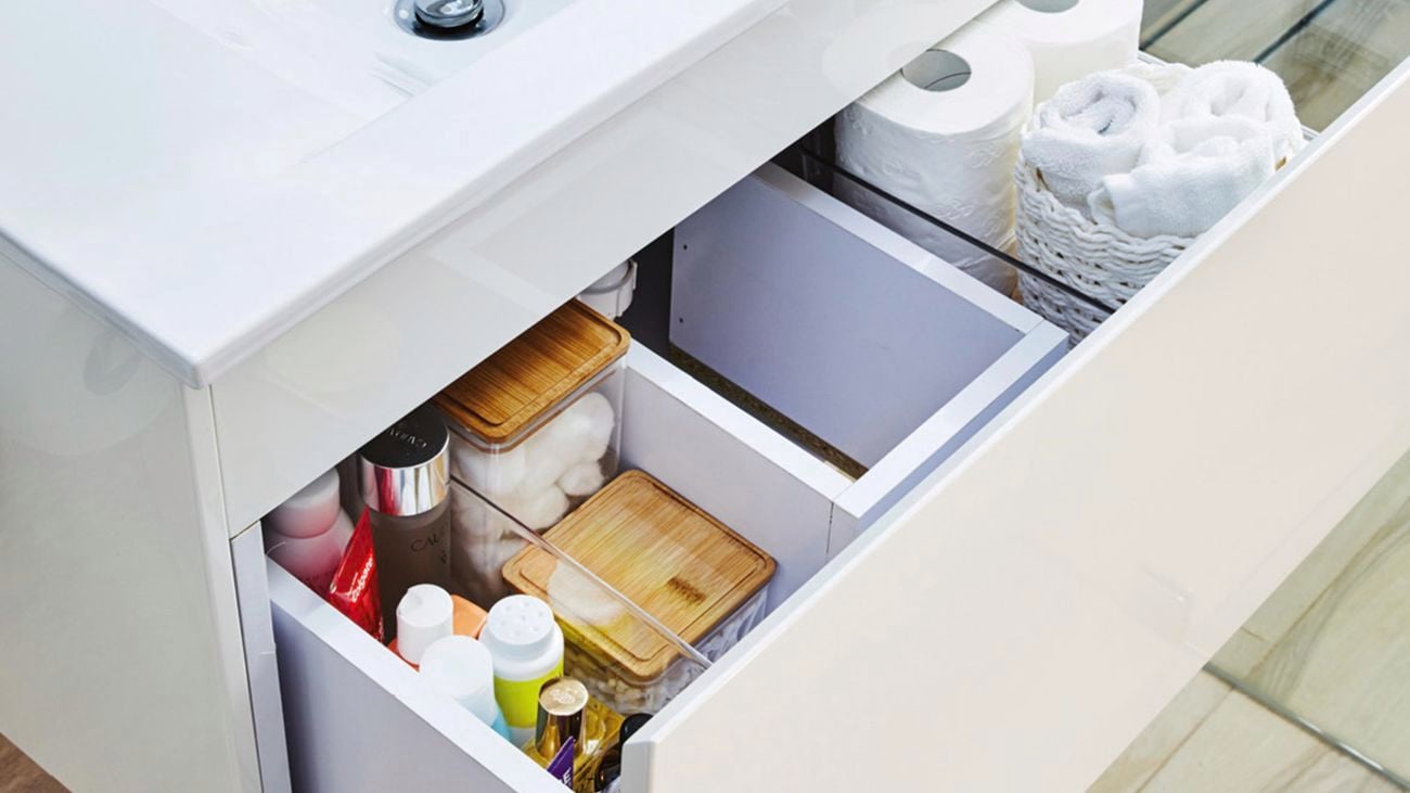 Opened vanity drawer organised by dividers housing bathroom lotions, toilet paper and towel.