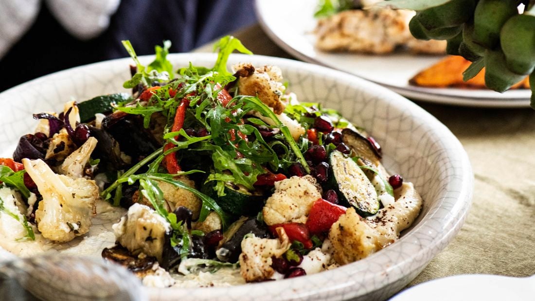 A closed up shot of a dish of Mediterranean vegetables (zucchinis, eggplants, cauliflowers, capsicums and rocket leaves) with garlic and hummus.