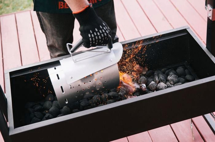 Person pouring hot charcoal briquettes into a smoker