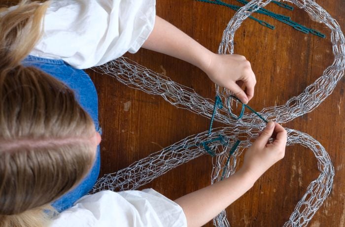Birds-eye view of lady tying wire pieces together using cable ties to form bow shape.
