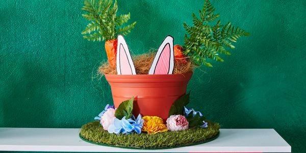 A Bunnings straw hat decorated with artificial turf, a plastic pot and faux carrots, flowers and bunny ears for Easter.