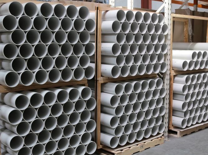 Stacks
  of white PVC pipes neatly arranged and stored on wooden pallets in a
  warehouse or storage facility