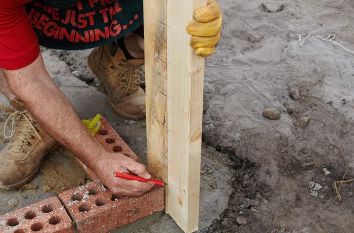 Person marking up two timber plinths that are sitting next to a row of bricks.
