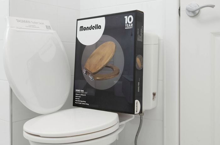 A bathroom with a toilet and a packaged Mondella wooden seat 