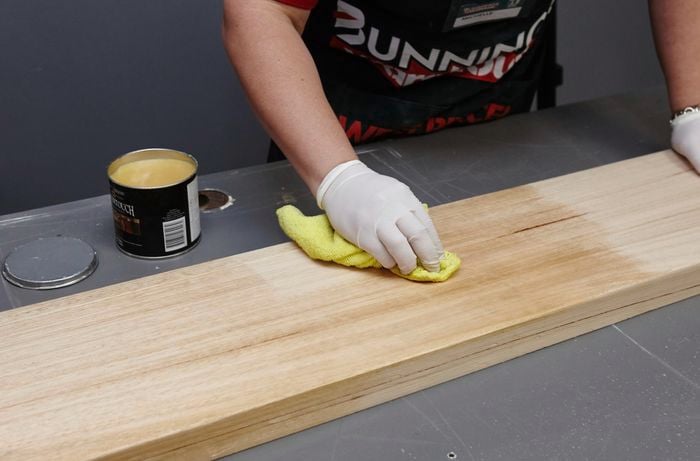 Person wearing gloves using a cloth to varnish a timber book shelf.