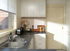 A bright, modern kitchen features white cabinets with gold handles, a double sink, and neatly arranged decor on the countertop