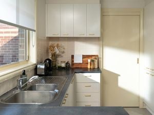 A bright, modern kitchen features white cabinets with gold handles, a double sink, and neatly arranged decor on the countertop