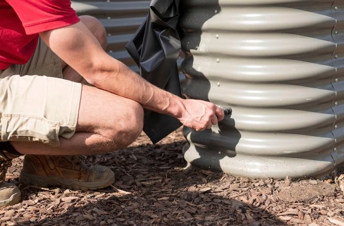 A person in a red T-shirt is installing an overflow outlet on the side of the garden bed.