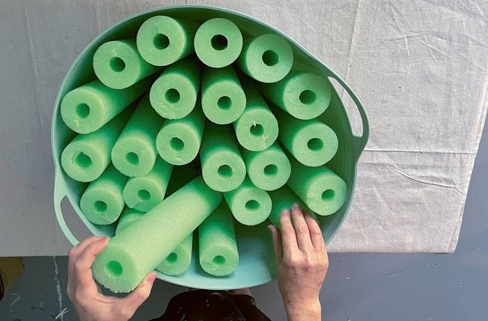 Hands inserting green pool noodle pieces into a light green tub.