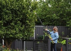 Lady using a pole pruner to trim hedge