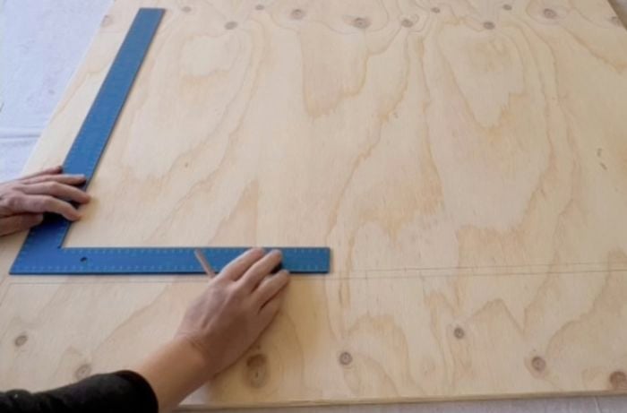 Hands using a combination square ruler to measure angles on piece of plywood.