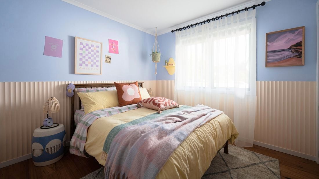 A stylish and functional teenage bedroom with colourful bedding and a decorative rug on hardwood flooring.