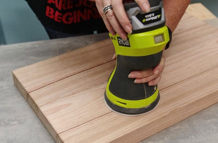 A person sanding a cutting board with an orbital sander