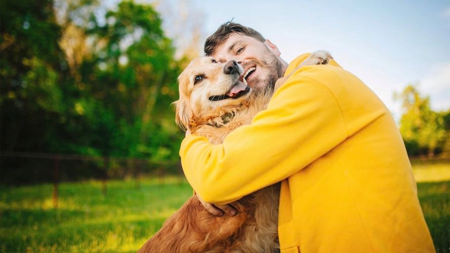 A man in a yellow jacket hugging a Golden Retriever.