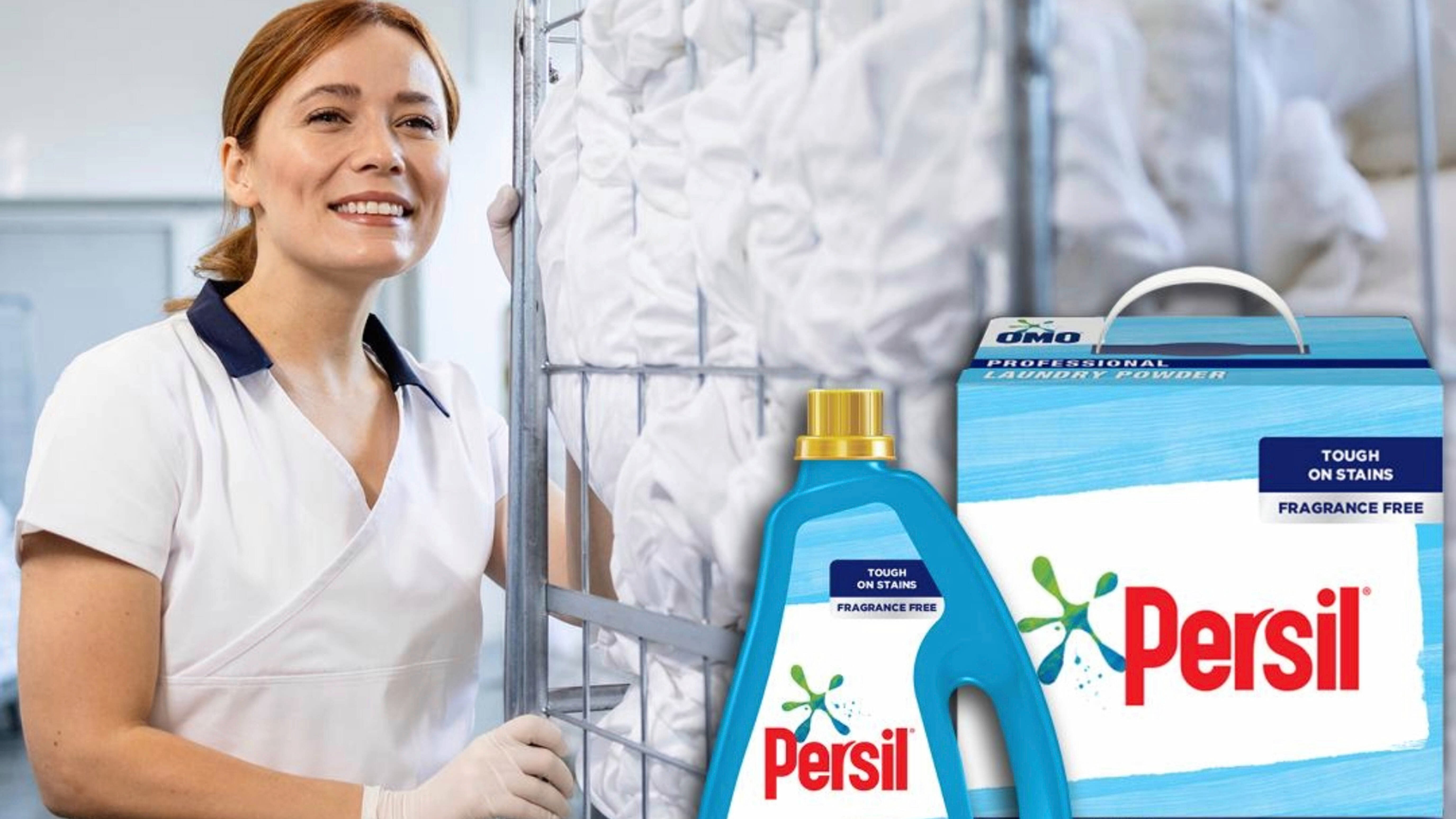 A woman in a white uniform pushing a full laundry trolley with a bottle of Persil laundry liquid and a box of Persil laundry powder in the foreground