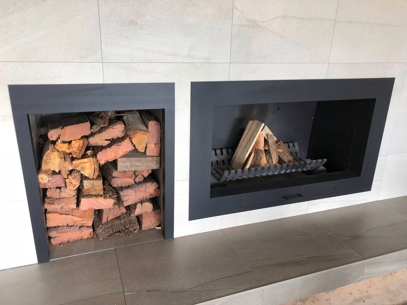 Modern fireplace with stacked firewood and prepared logs on metal grate.