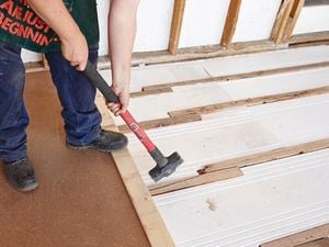 Person knocking chipboard panel into place with a sledgehammer